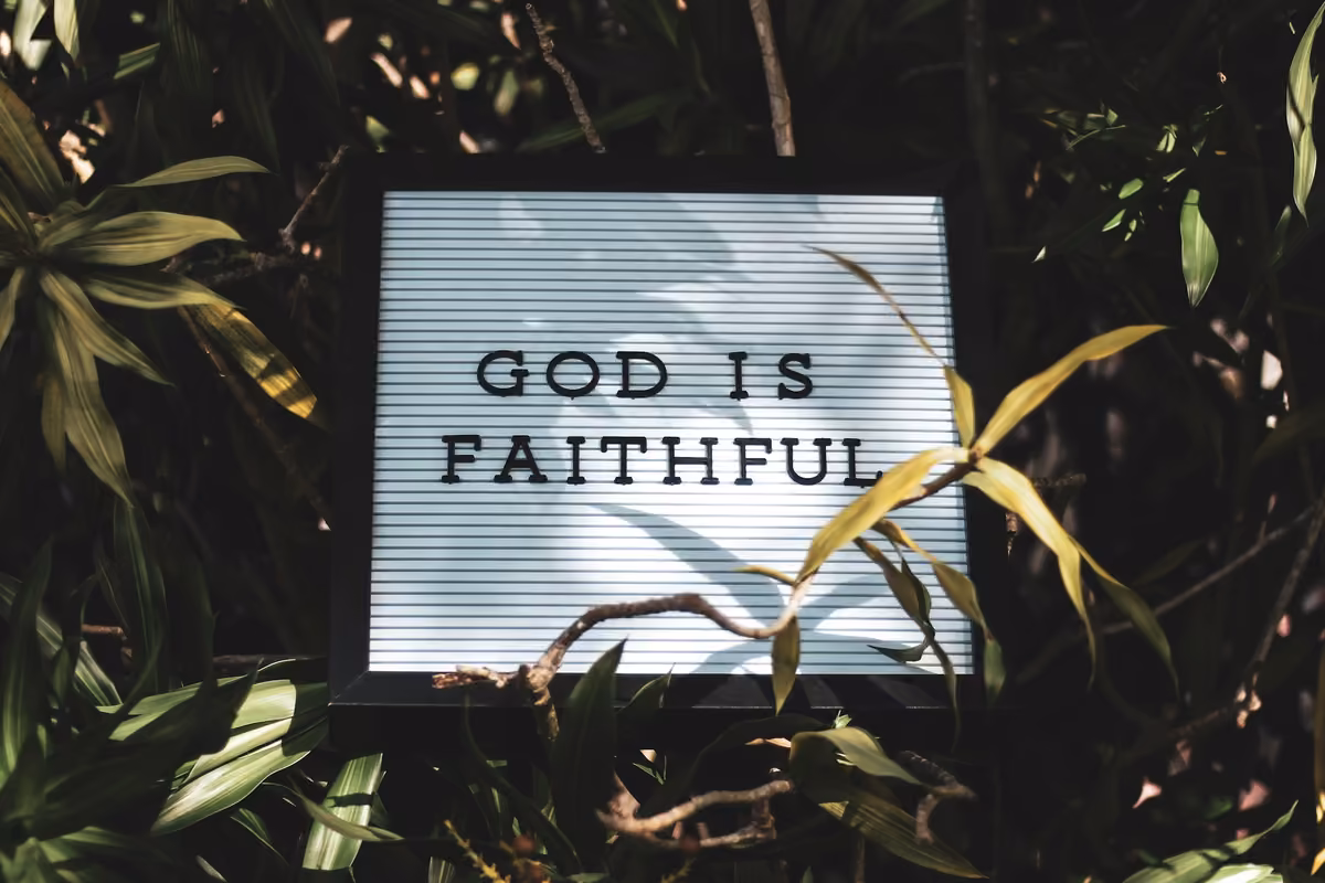 Felt board with square letters that form the phrase «GOD IS FAITHFUL», surrounded by lush green leaves.