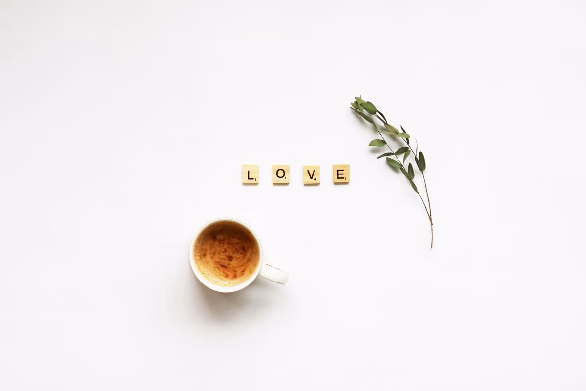 Wooden tiles spelling out the word 'LOVE' accompanied by a cup of coffee and a green sprig on a white background.