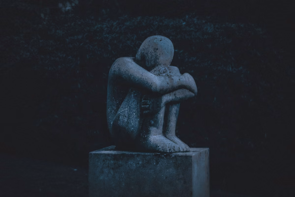 Statue of a person curled up in a fetal position on a pedestal in the dark.