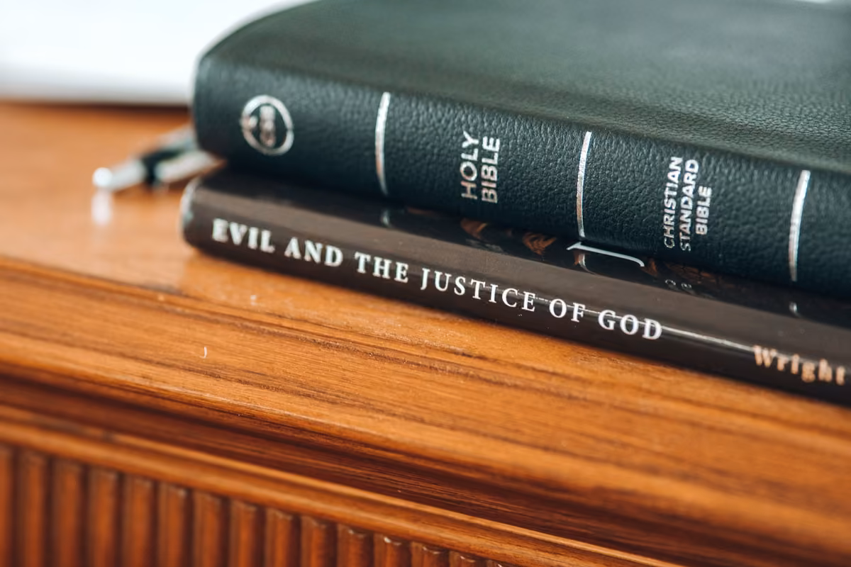 A black leather Bible resting on the book ‘Evil and the Justice of God’ by N.T. Wright atop a wooden piece of furniture.