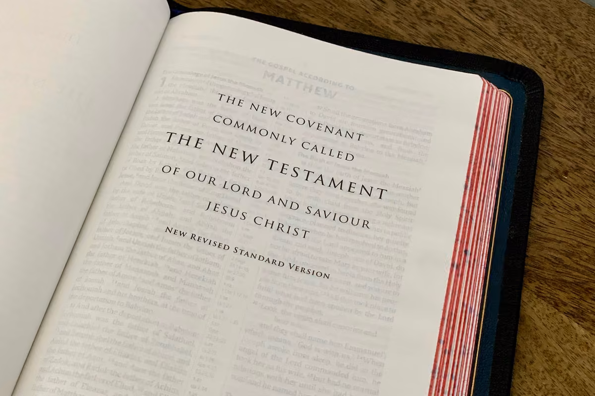 Open Bible showing the New Testament title page in English on a wooden table.