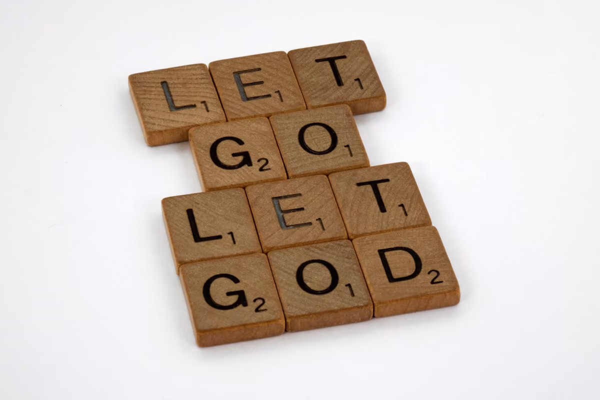 Wooden Scrabble tiles arranged on a white background forming the phrase Let Go, Let God.