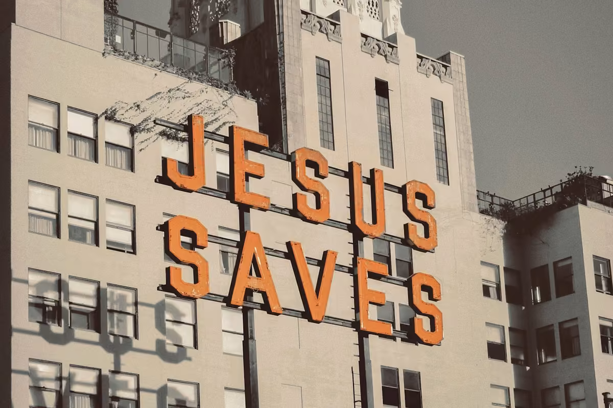 Vintage orange neon sign on an old building with the inscription ‘JESUS SAVES’.