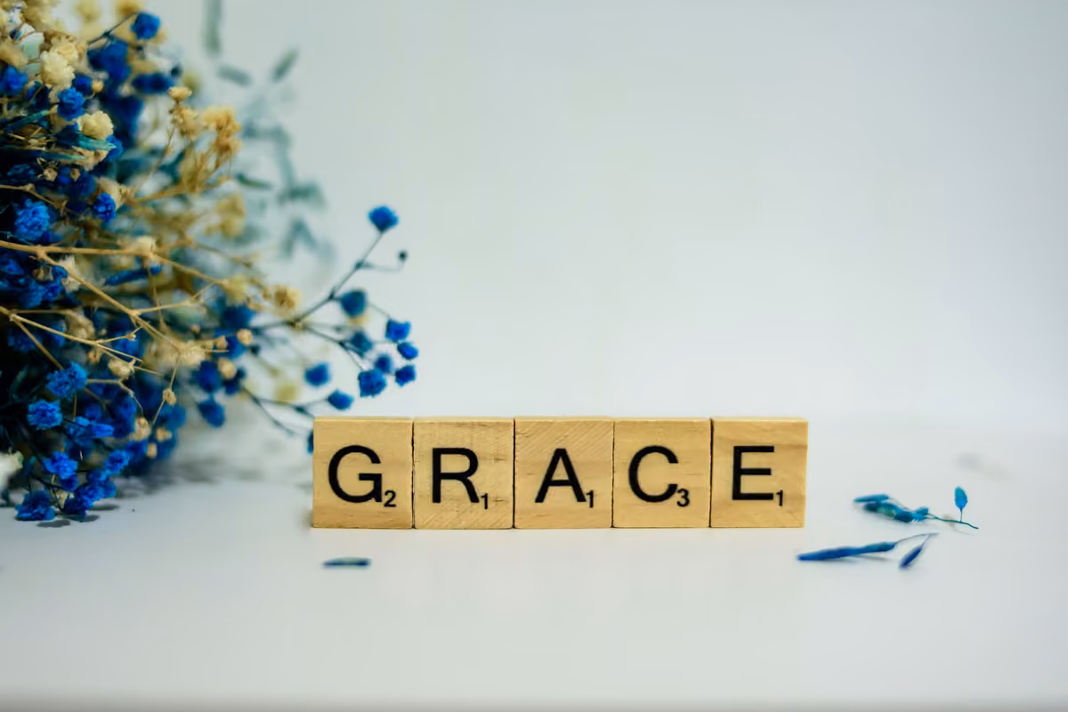 Wooden Scrabble tiles forming the word 'GRACE' next to a bouquet of dried blue and white flowers.