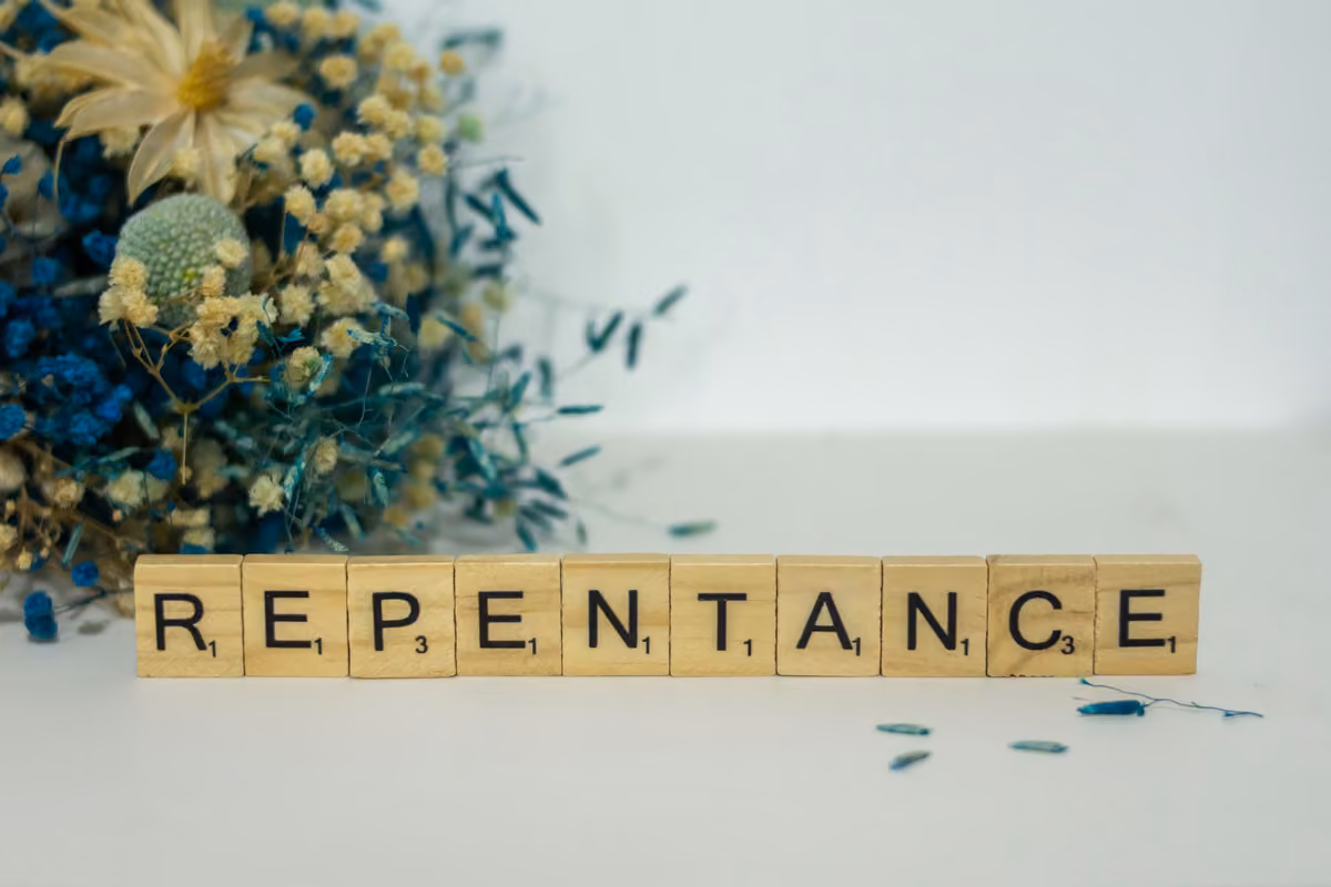 Wooden tiles spelling the word 'REPENTANCE' beside an arrangement of dried blue and yellow flowers on a white surface.