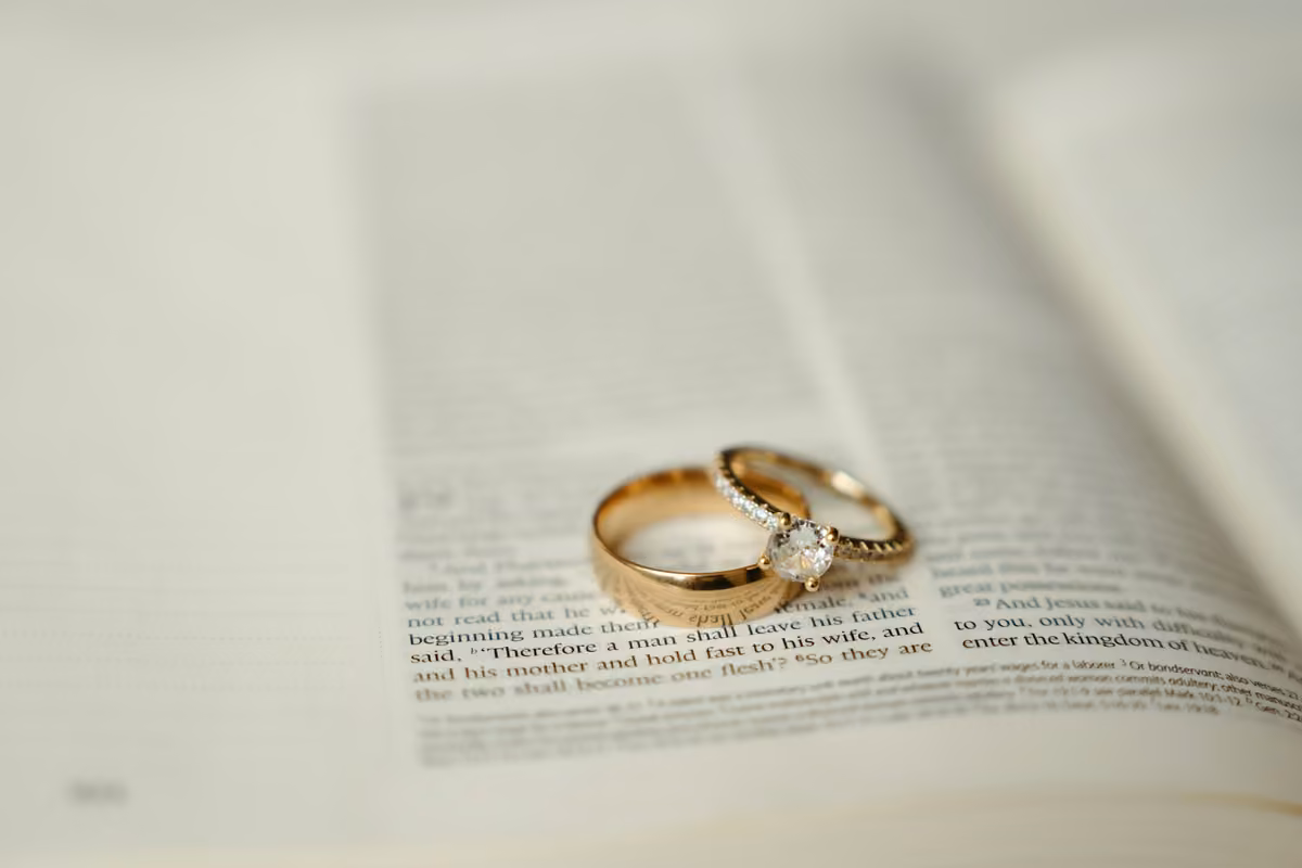 Two gold wedding rings resting on an open biblical passage speaking about marriage.