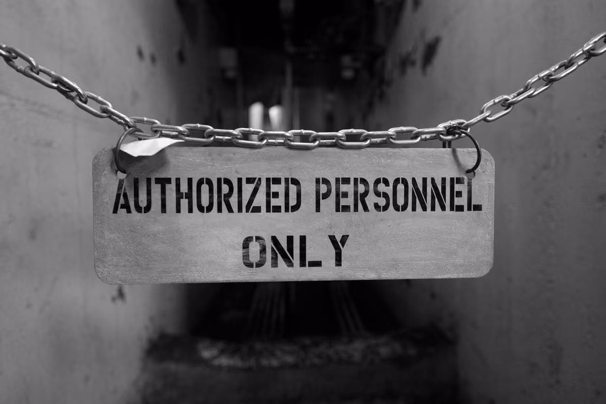 Black and white metal sign hanging from a chain with the text «AUTHORIZED PERSONNEL ONLY» in front of an industrial aisle.
