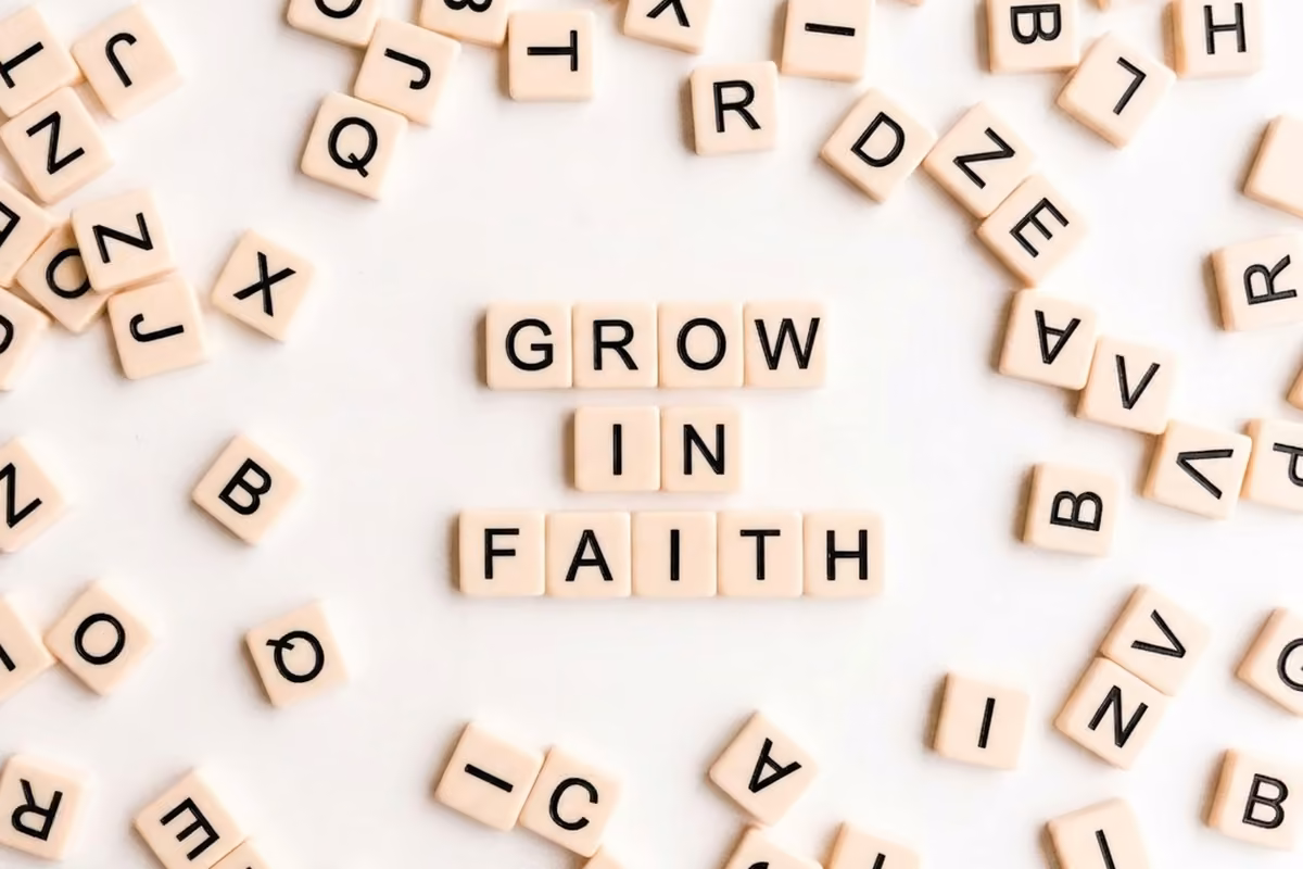 White plastic letter tiles forming the message 'GROW IN FAITH' surrounded by scrambled letters on a white background.