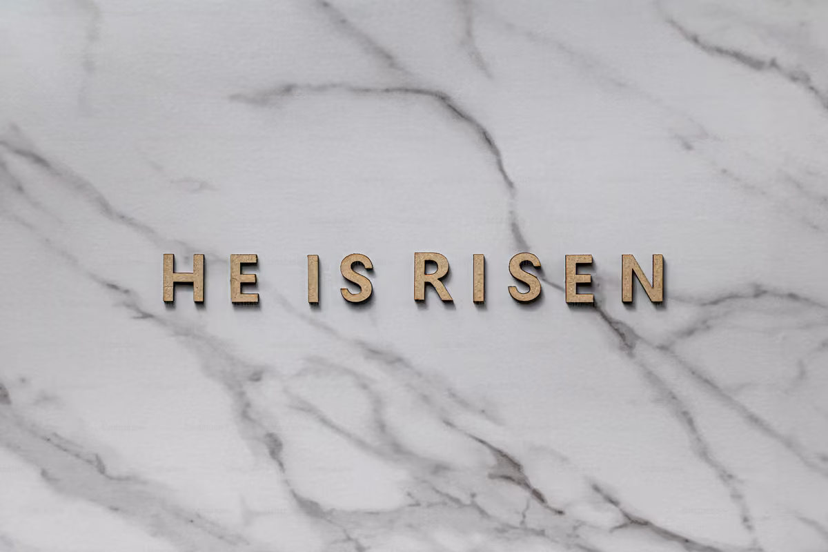 Wooden letters forming the phrase 'HE IS RISEN' placed on a white marble surface with gray veins.